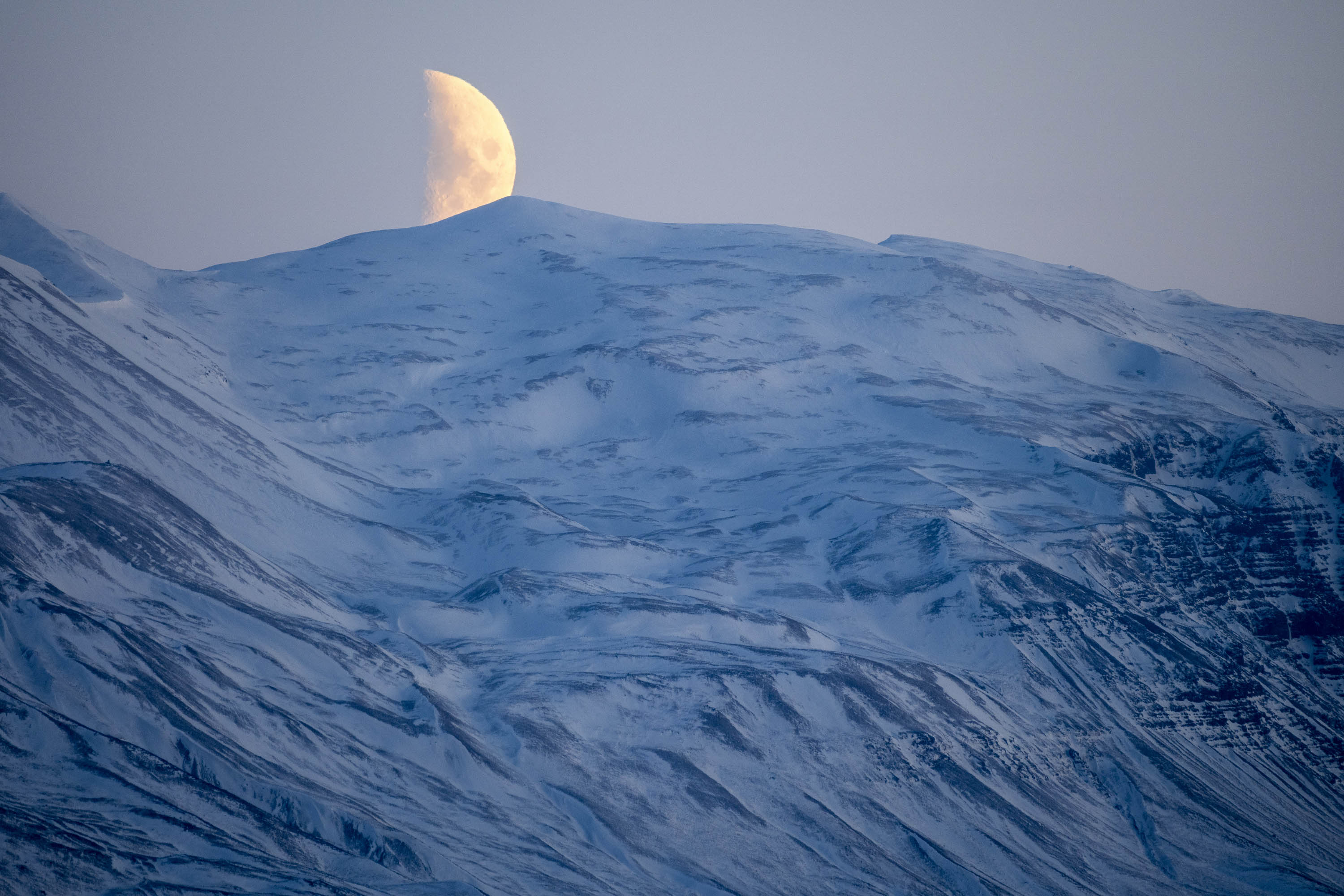 Half-moon setting over snowy mountaintops in the Northwestern Region of Iceland.