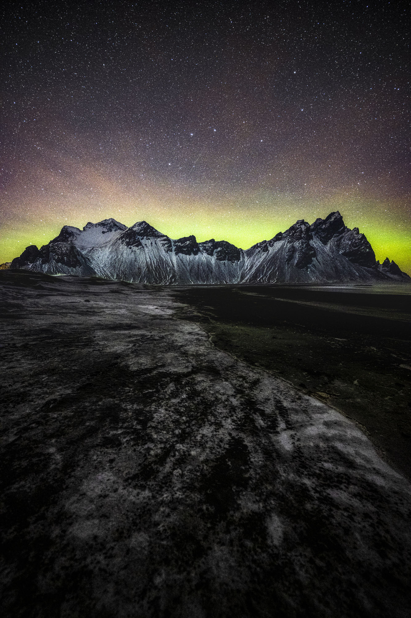 Northern Lights radiate behind snowy mountains in the night sky near Stokksnes in Southern Iceland.