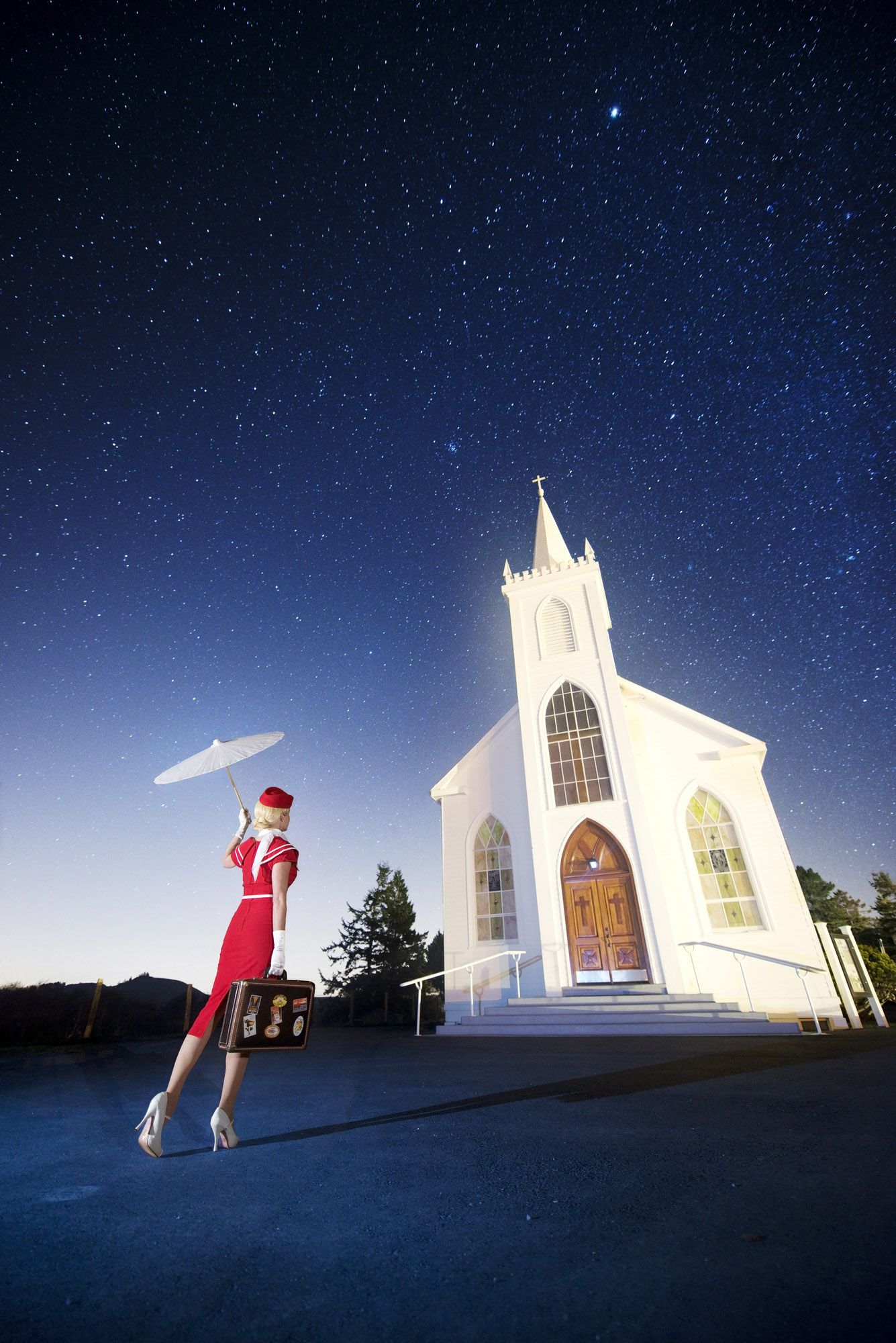 Woman in a red approaches a church under a starry night sky in Bodega, California.